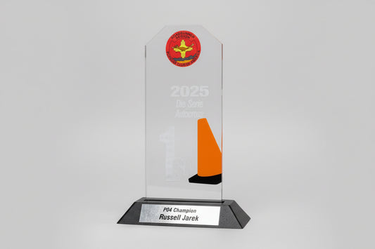 A trophy with '2025 Die Serie Autocross' and '1st' engraved on it, featuring an orange traffic cone and a logo at the top.