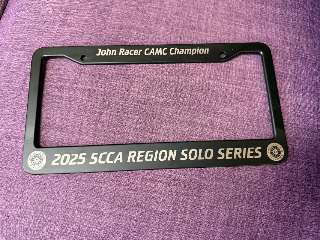 Black license plate frame with racing achievements on a purple fabric background