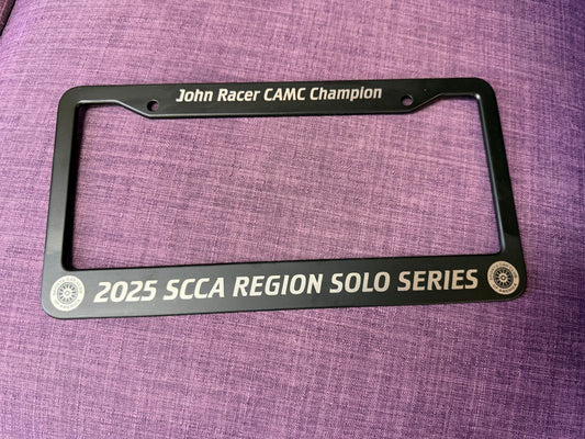 Black license plate frame with racing achievements on a purple fabric background